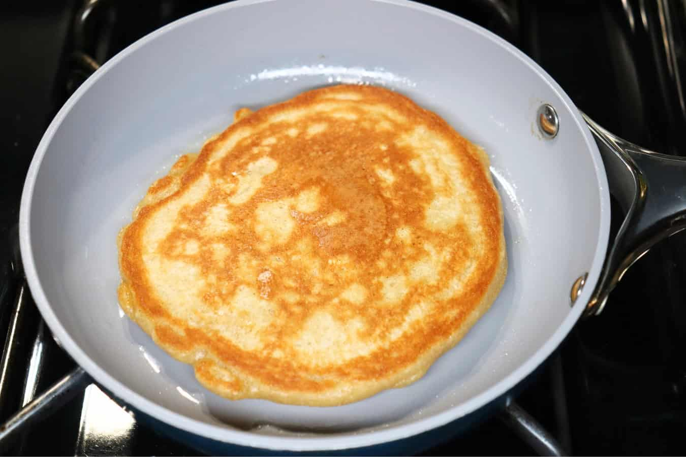 A golden-brown pancake cooking in a nonstick skillet, shown after being flipped.
