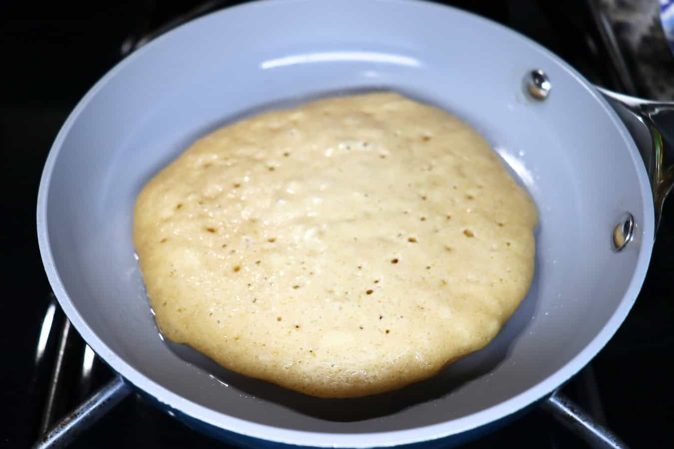 A pancake cooking in a nonstick skillet, with bubbles forming on the surface, indicating it's ready to flip.