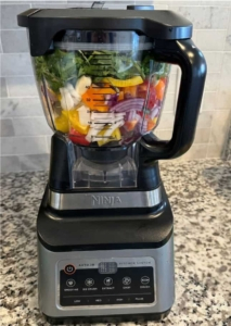 A blender filled with fresh vegetables to make a vibrant Dominican sofrito (sazón) base.