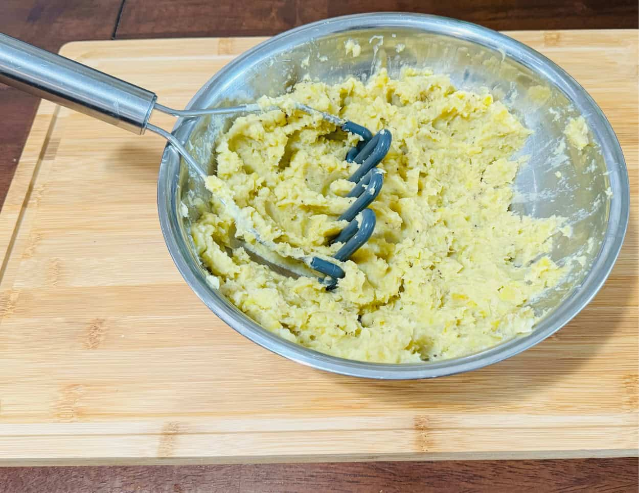 Partially mashed plantains in a mixing bowl with a potato mas