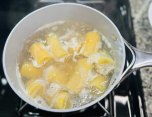 Chunks of green plantains boiling in a pot of salted water on a stovetop.