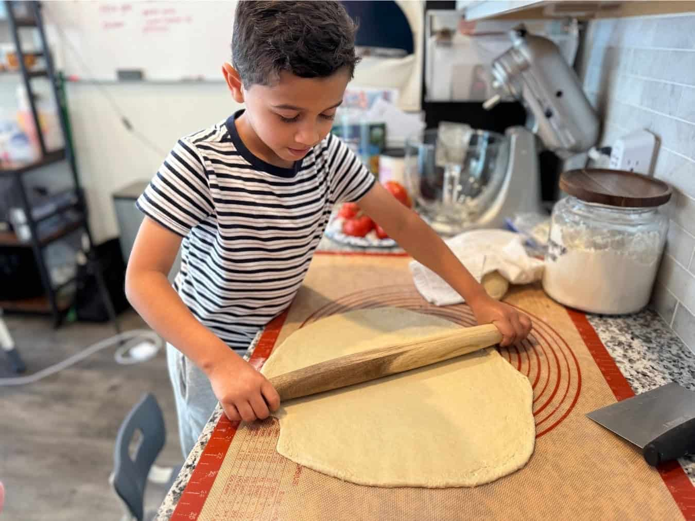 Liam is spreading pizza dough, showing the benefit of cooking with your kids.