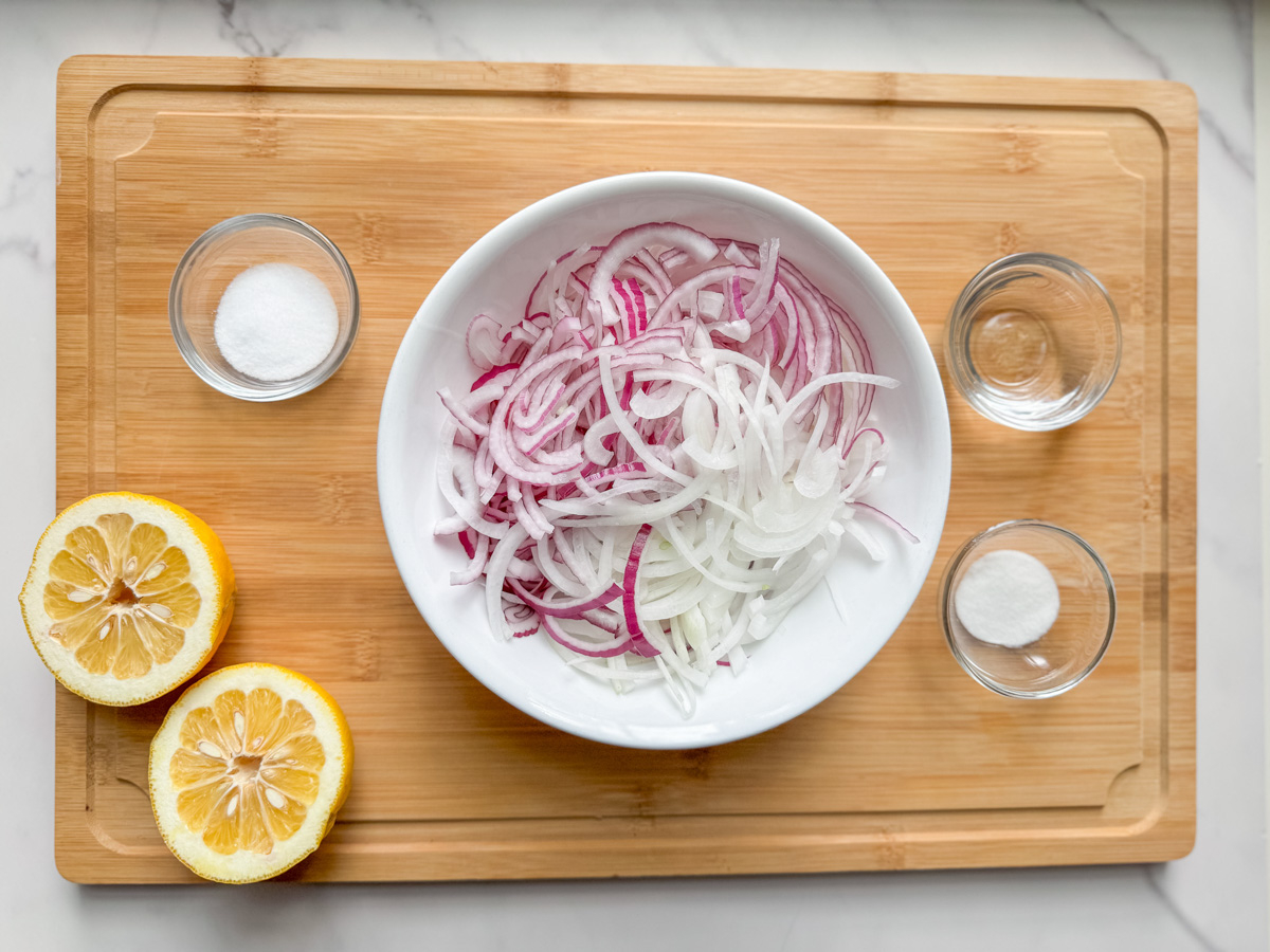 Dominican sautéed onions ingredients: sliced red and white onions, sour orange, vinegar, sugar, and salt on a board