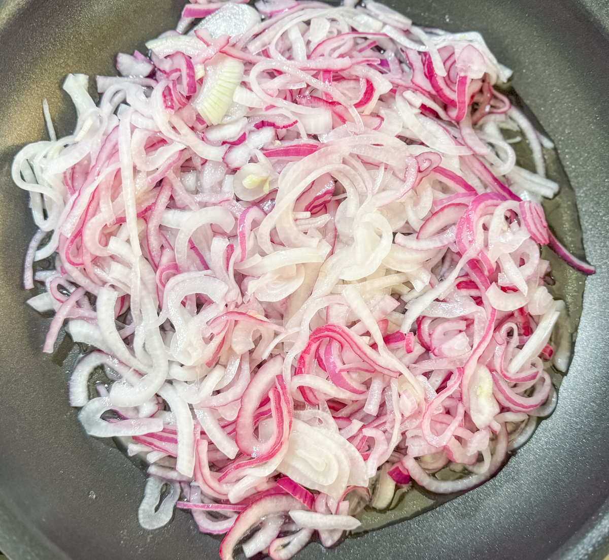 Dominican sautéed onions—marinated onions added to a skillet with oil, ready to cook