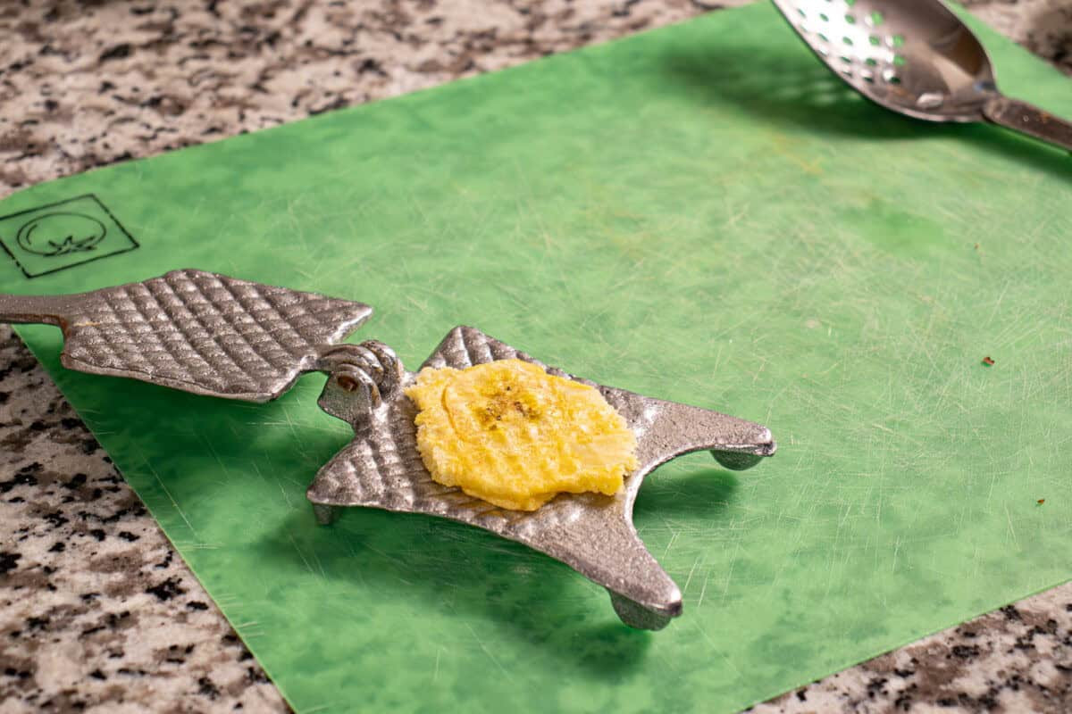 Fried plantain chunk being smashed with a tostonera