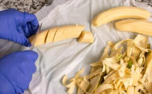 Peeled plantains being cut into chunks for frying, with the peels set aside.