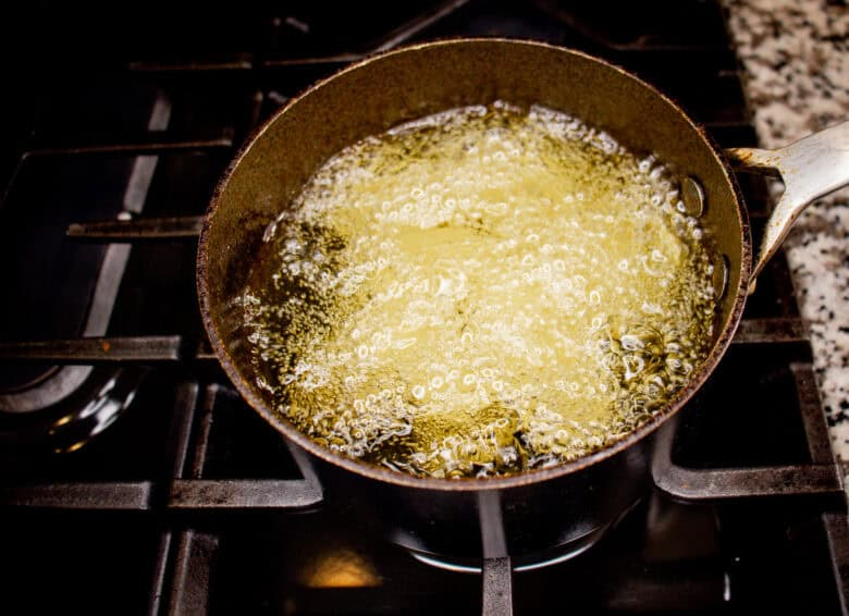Hot oil bubbling in a small pot on the stove, plantain chunks are frying inside