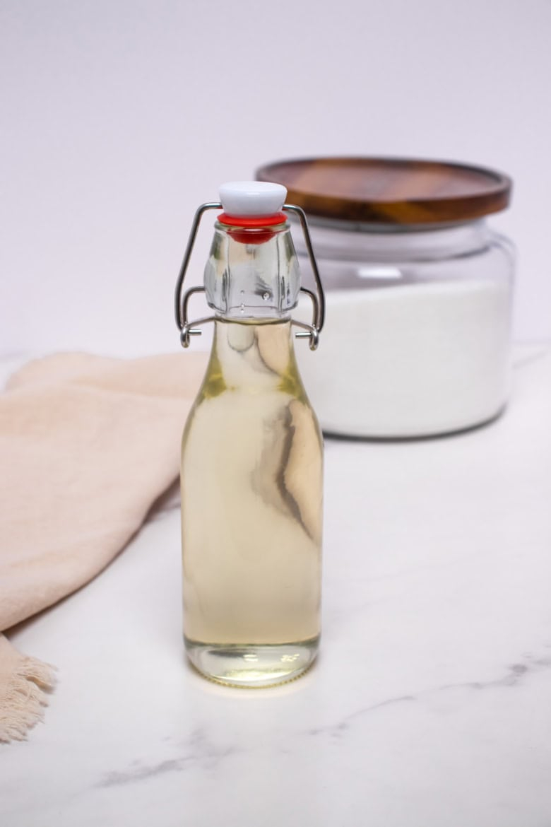 Bottle of homemade simple syrup with a sugar jar in the background