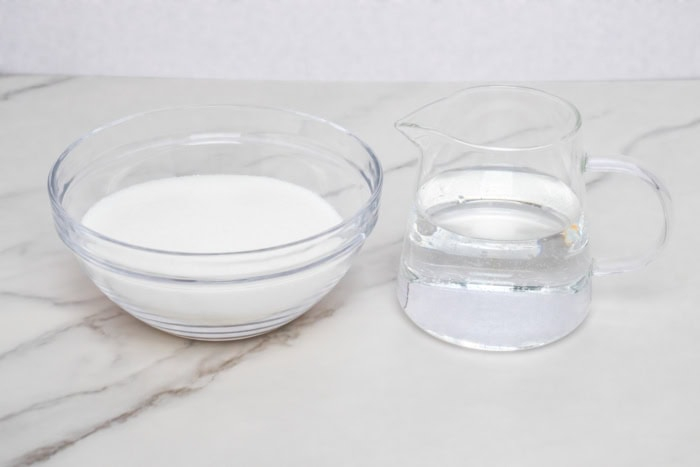 Granulated sugar and water measured for a homemade simple syrup recipe