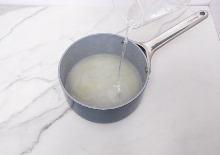 Water being poured into a saucepan to make homemade simple syrup