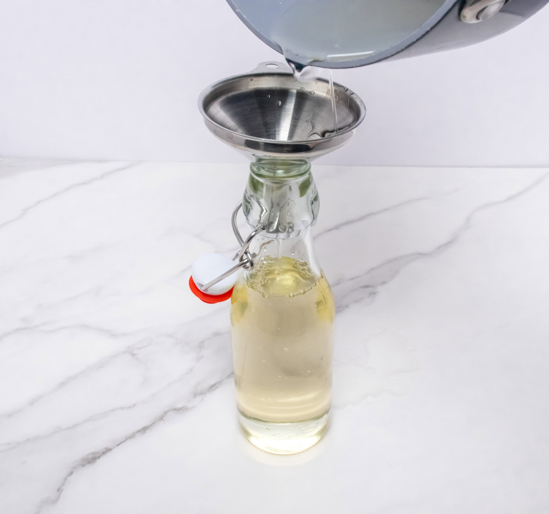 Simple syrup being poured into a glass bottle through a funnel