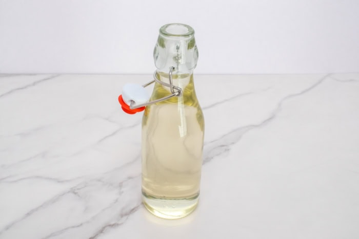 Finished simple syrup in an open glass bottle on a white marble counter