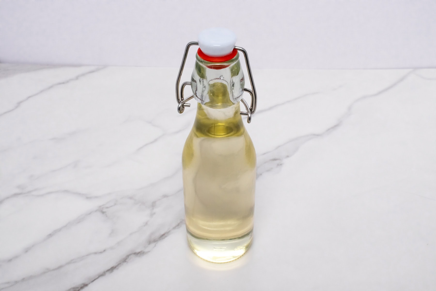 Glass bottle filled with homemade simple syrup on a white marble counter