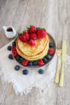 Hero image of fluffy pancakes topped with berries on a plate with syrup pitcher and gold utensils