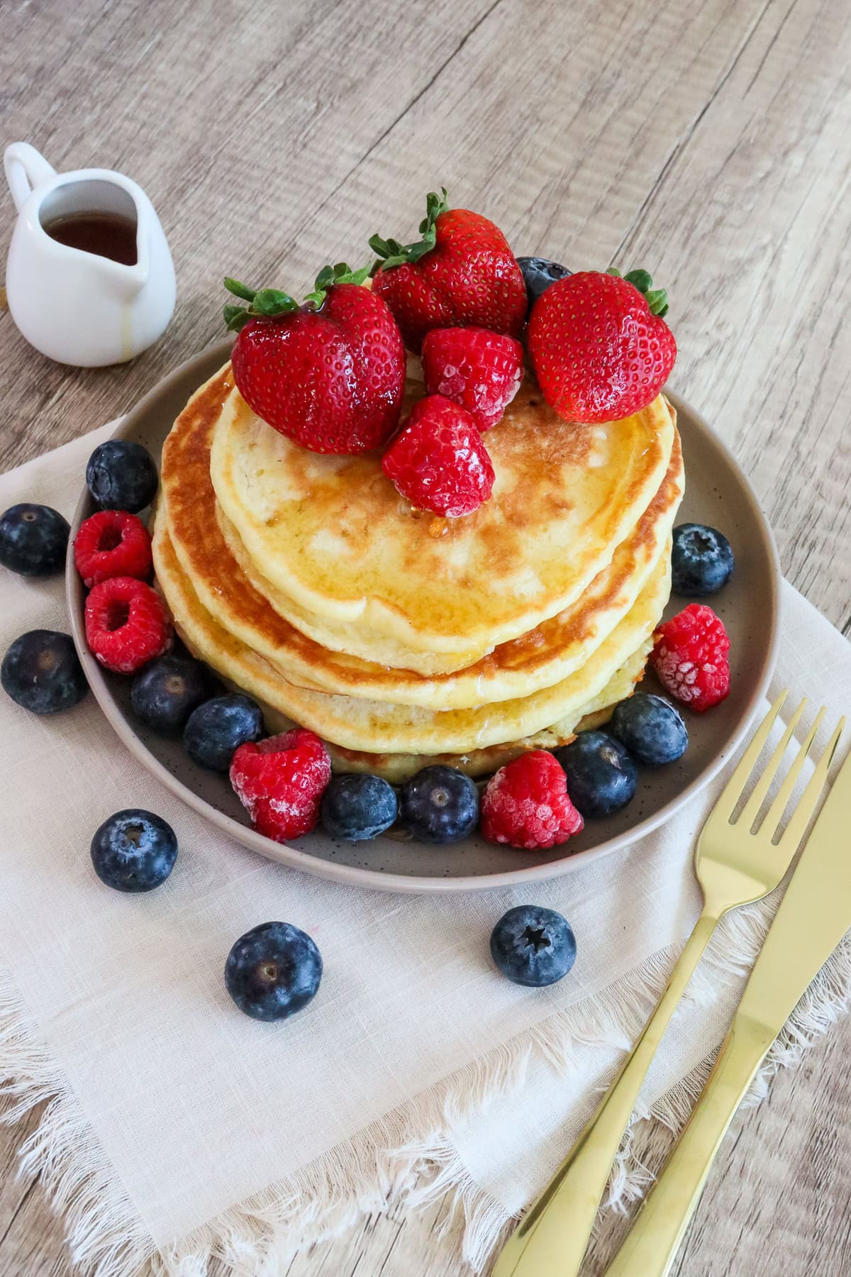 Golden fluffy pancakes topped with fresh strawberries and raspberries with syrup drizzled over the top