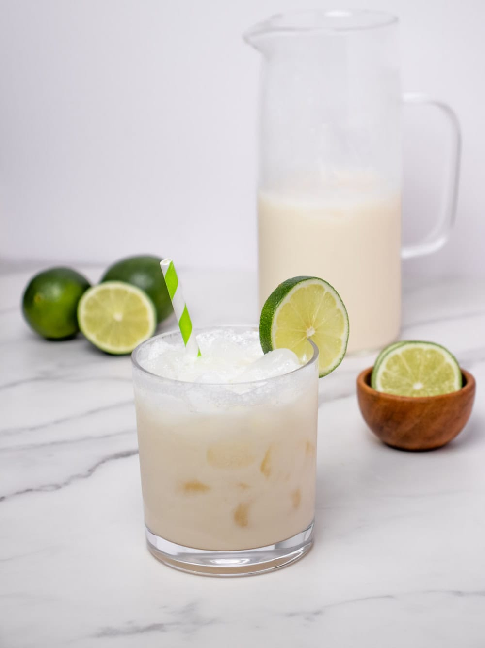 Morir Soñando de Limón over ice with lime garnish, fresh limes, and pitcher in background.