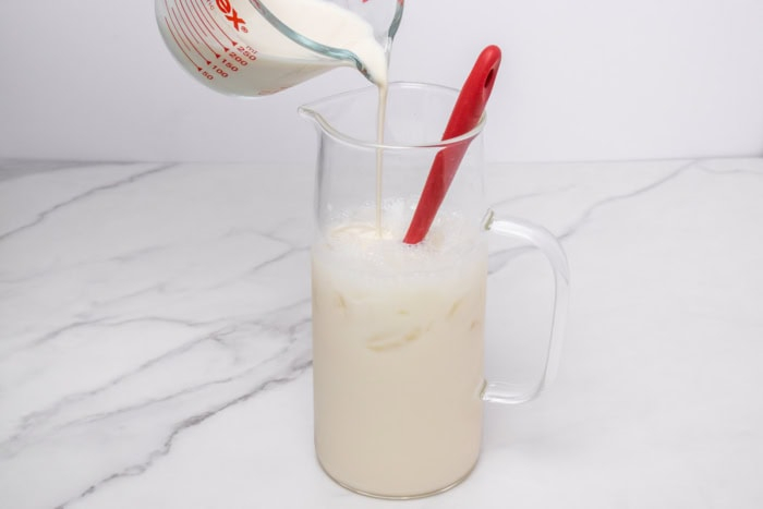 Evaporated milk being poured into an iced lime mixture in a pitcher for Morir Soñando de Limón.