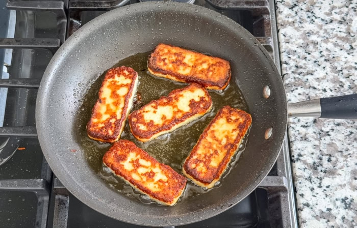 Deeply browned queso de freír slices finishing in a skillet