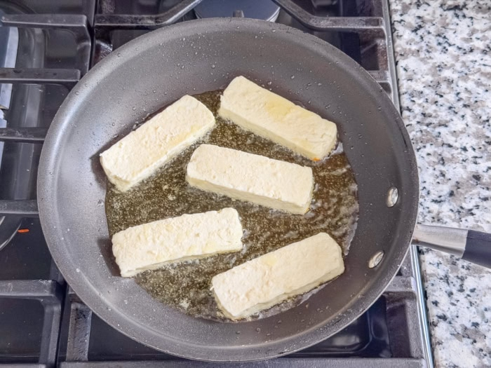 Five flour-coated queso de freír slices sizzling in oil before browning