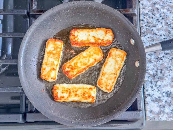 Five Dominican fried cheese slices with golden-brown sides in a skillet