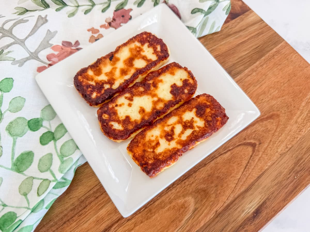 Three golden-brown pieces of Dominican fried cheese on a white square plate